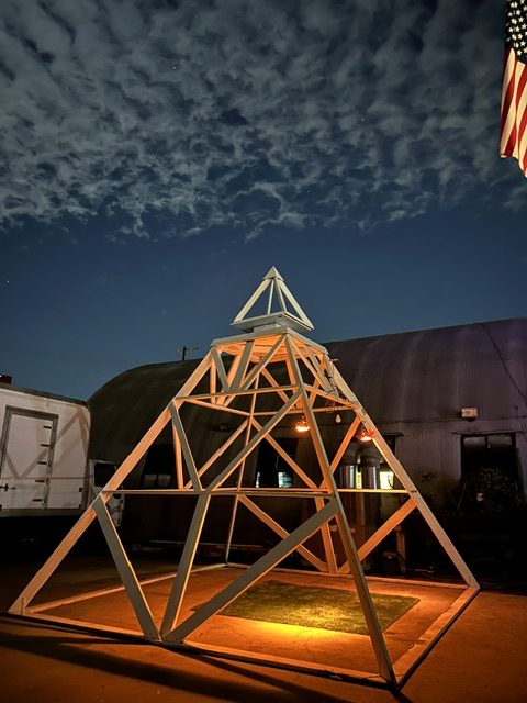 Wooden pyramid art structure at the Kitty Bus venue entrance at night