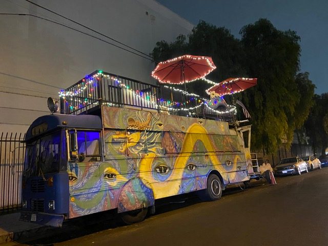 Kitty Bus exterior with psychedelic mural and rooftop umbrellas at dusk